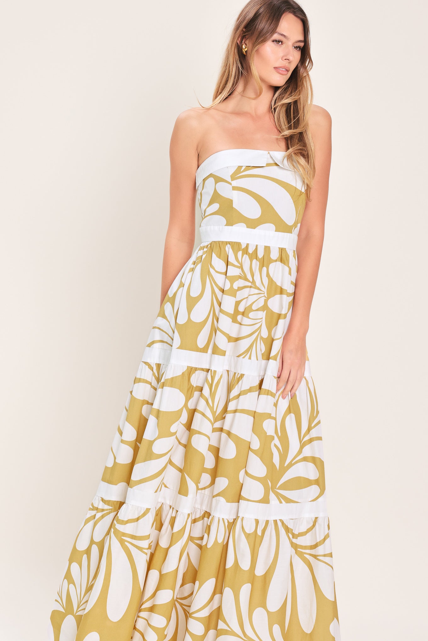 Woman wearing a beige and white  maxi dress featuring strapless neckline, tier skirt and back zipper closure | Flying Tomato