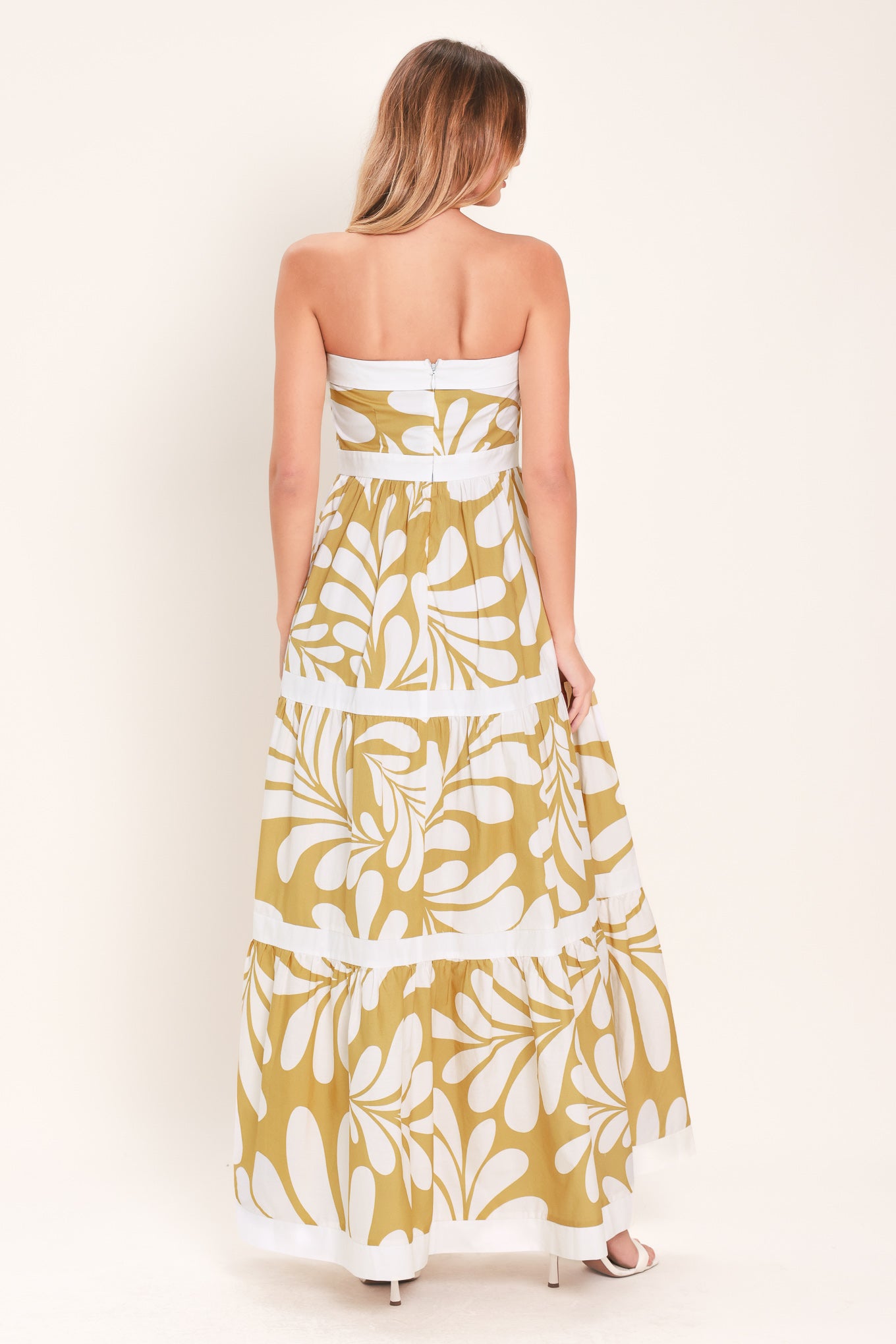 Woman wearing a beige and white  maxi dress featuring strapless neckline, tier skirt and back zipper closure | Flying Tomato