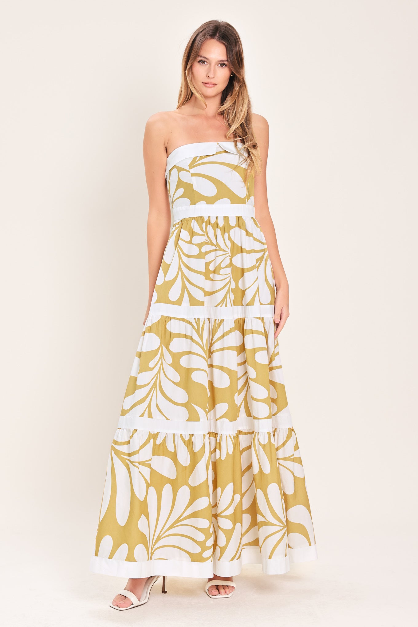 Woman wearing a beige and white  maxi dress featuring strapless neckline, tier skirt and back zipper closure | Flying Tomato