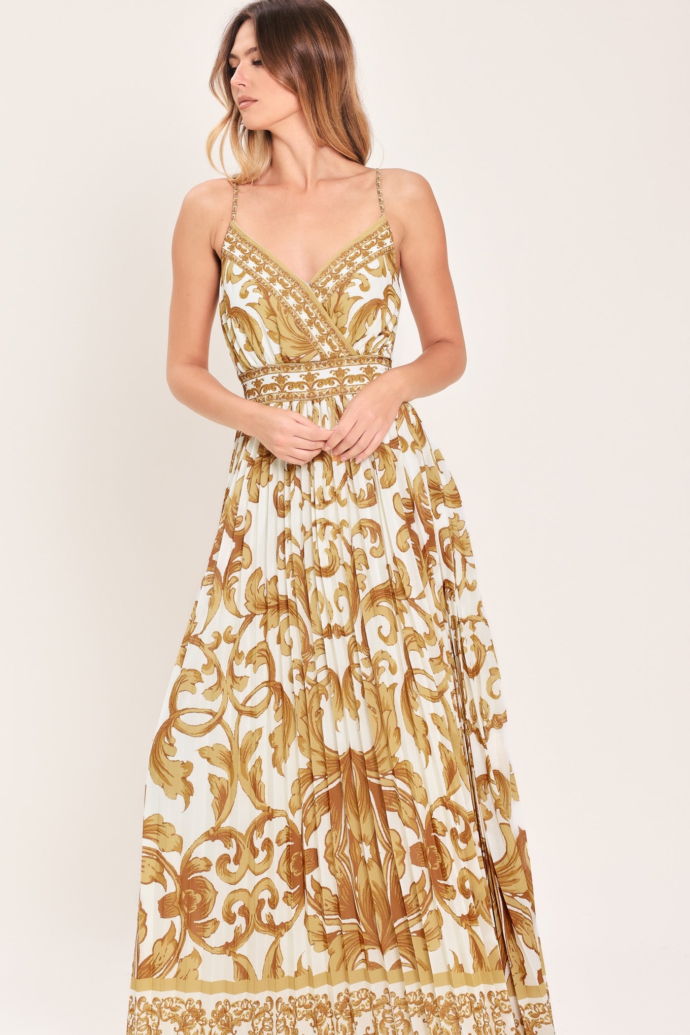 Woman wearing a gold and white baroque patterned maxi dress featuring surplice neckline, straps, pleated skirt and smocked back waistband | FLYING TOMATO