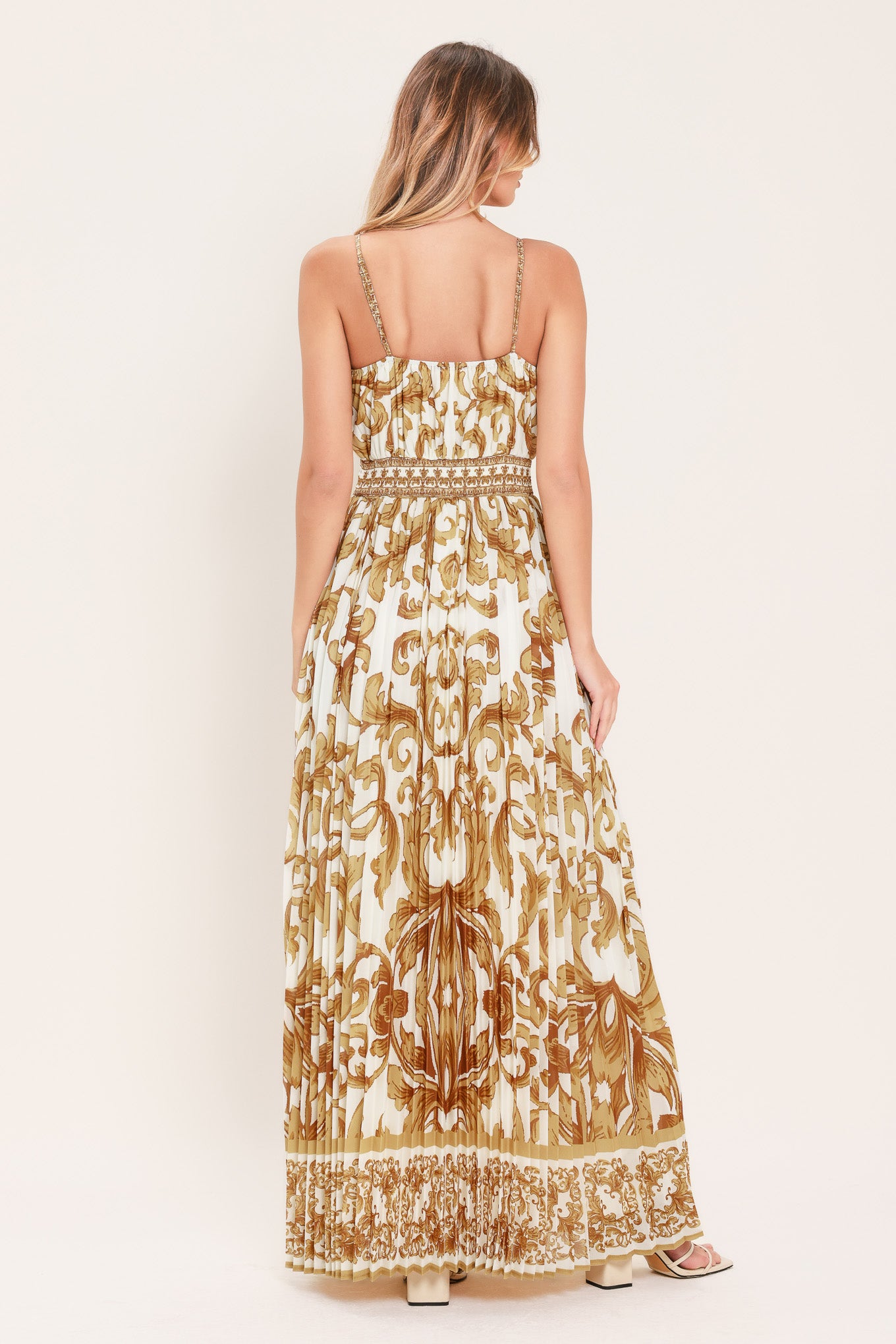 Woman wearing a gold and white baroque patterned maxi dress featuring surplice neckline, straps, pleated skirt and smocked back waistband | FLYING TOMATO