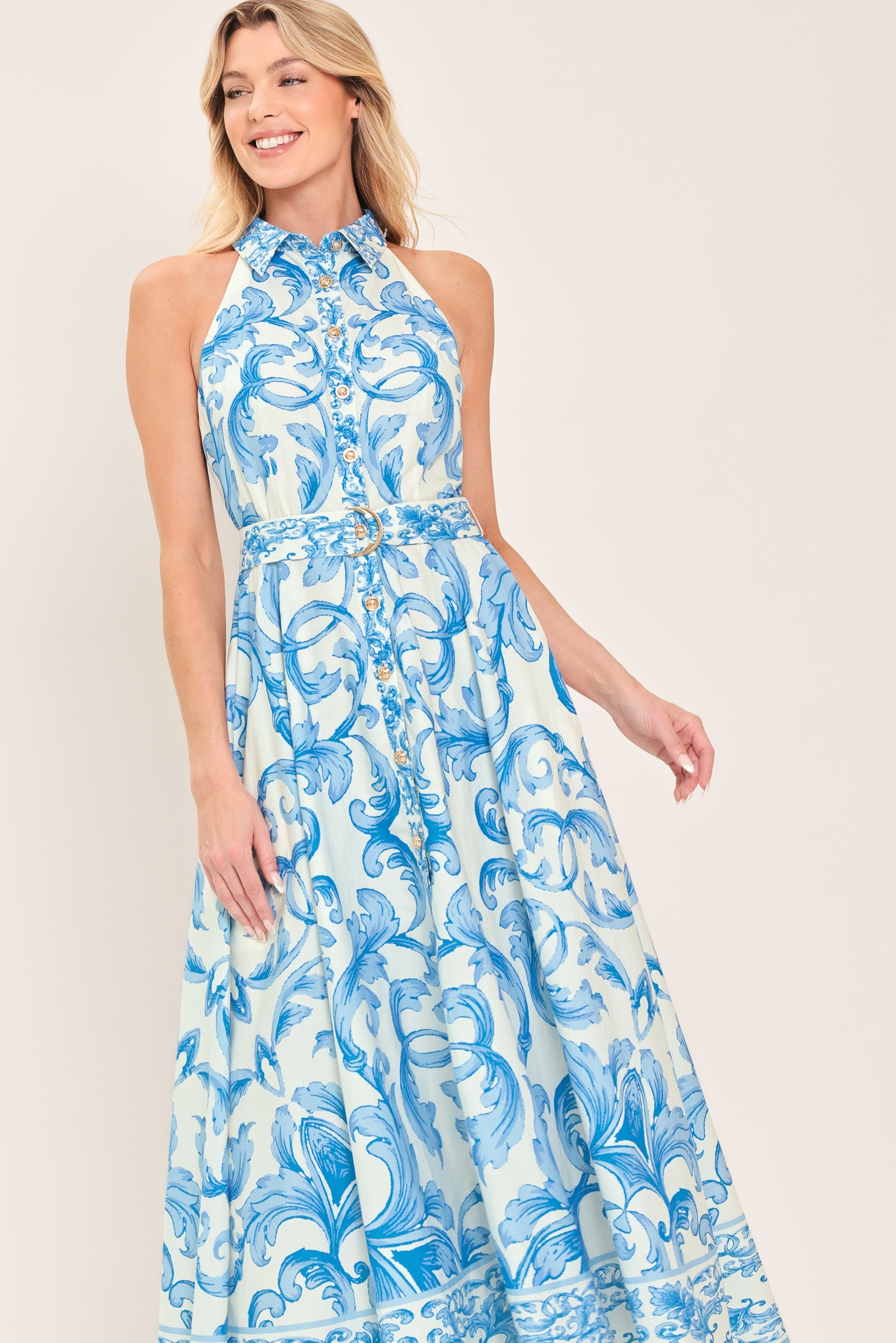 Woman wearing a blue and white patterned  maxi dress featuring collar, sleeveless, button down closure, self belt and full skirt  | Flying Tomato