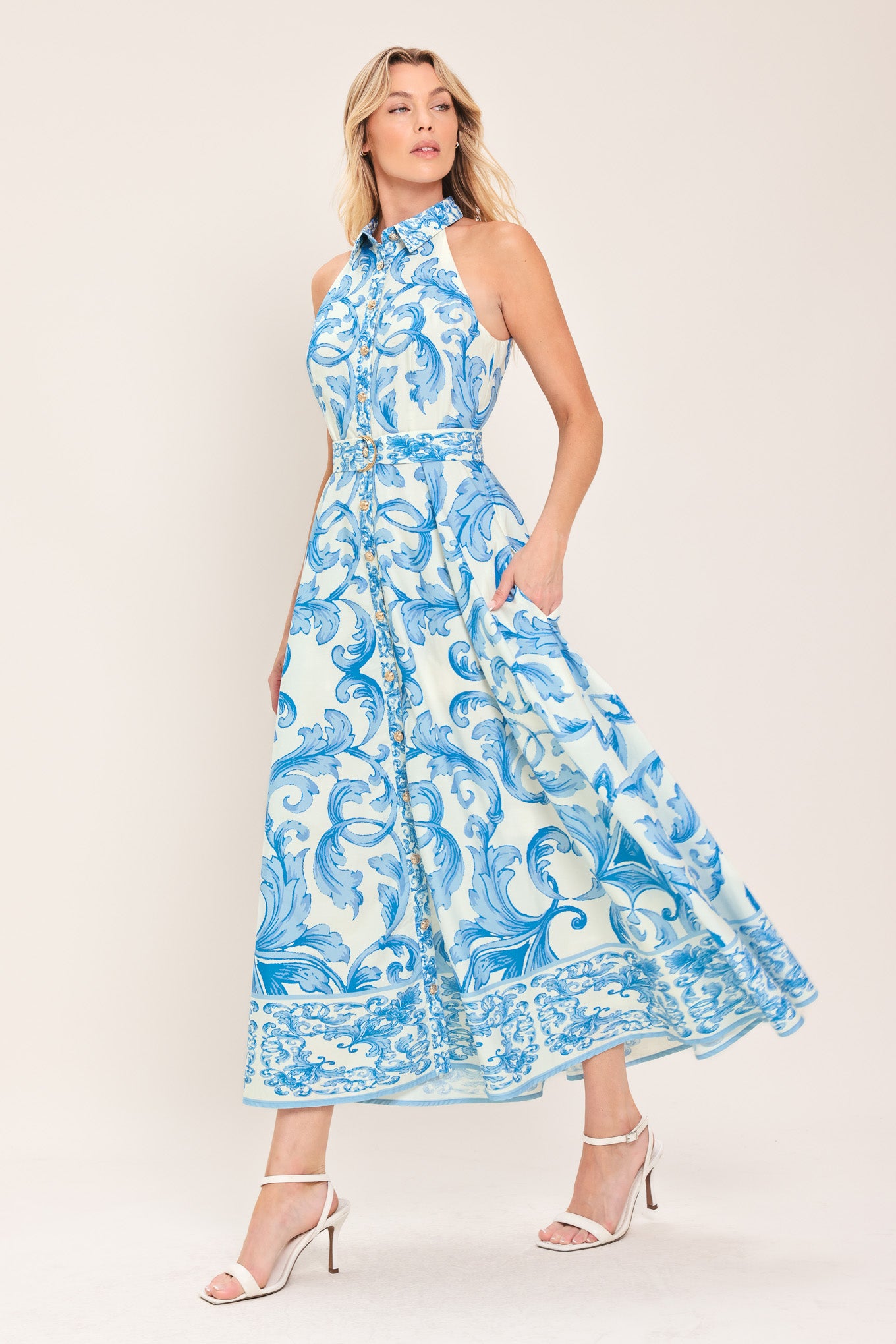 Woman wearing a blue and white patterned  maxi dress featuring collar, sleeveless, button down closure, self belt and full skirt  | Flying Tomato