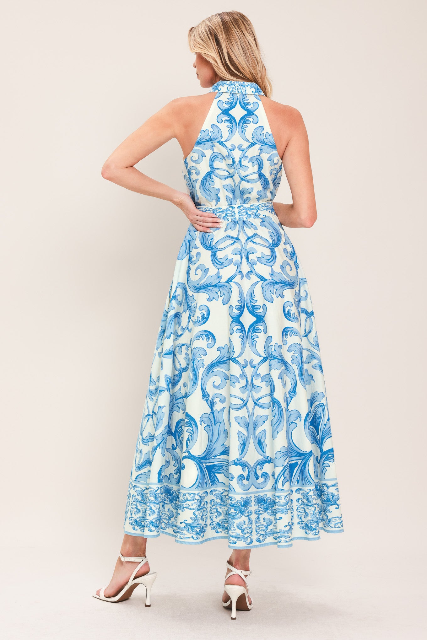 Woman wearing a blue and white patterned  maxi dress featuring collar, sleeveless, button down closure, self belt and full skirt  | Flying Tomato