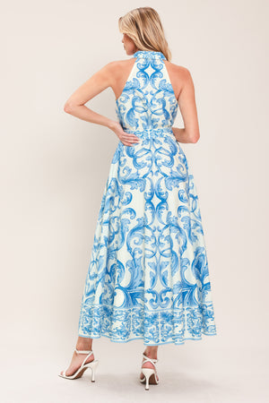 Woman wearing a blue and white patterned  maxi dress featuring collar, sleeveless, button down closure, self belt and full skirt  | Flying Tomato