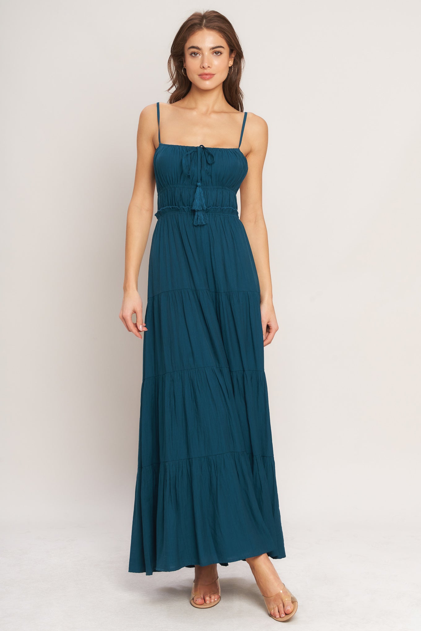 A solid woven maxi dress featuring straight neckline, front tie/tassel, straps, elastic at empire, tier skirt, bare back with straps