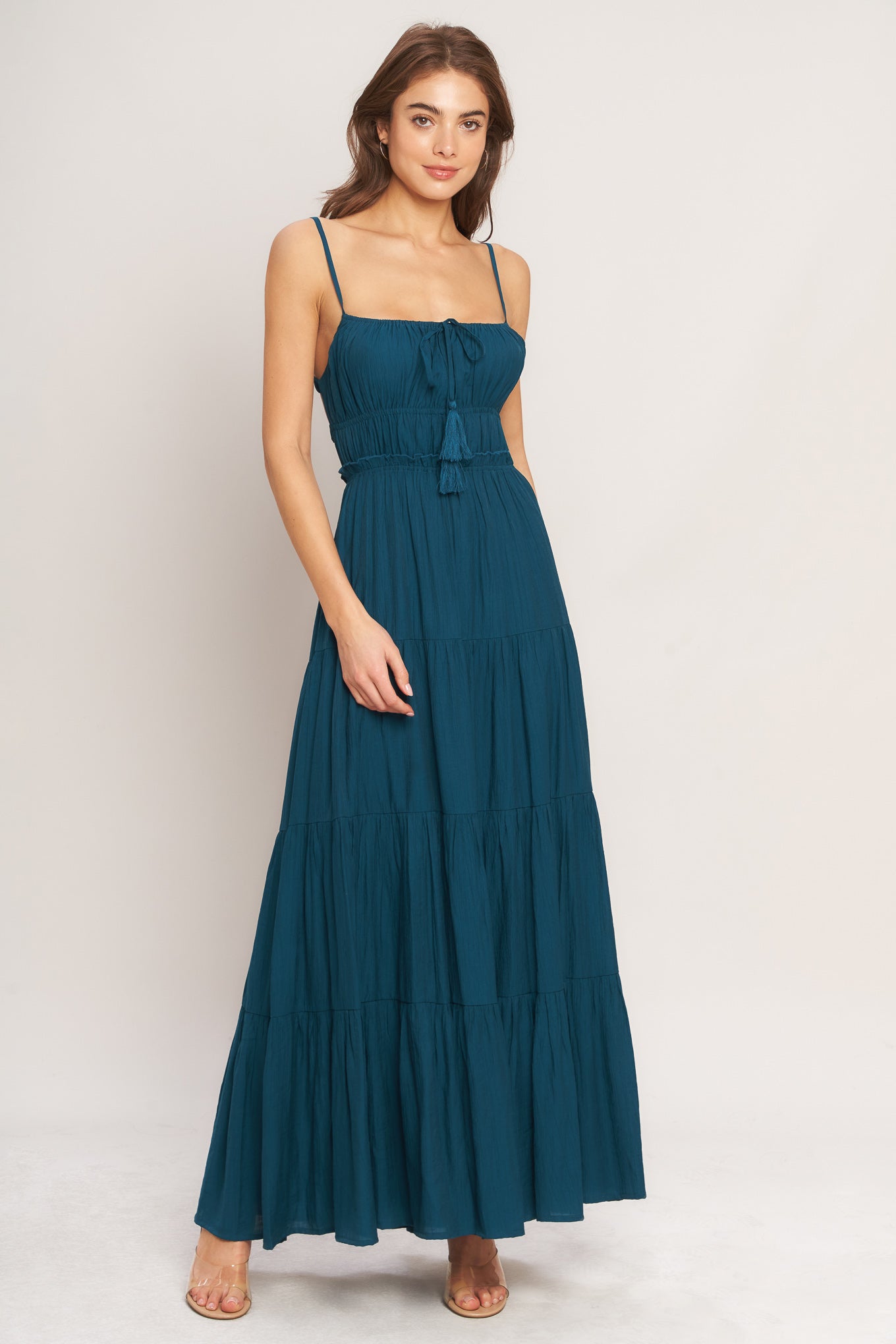 A solid woven maxi dress featuring straight neckline, front tie/tassel, straps, elastic at empire, tier skirt, bare back with straps