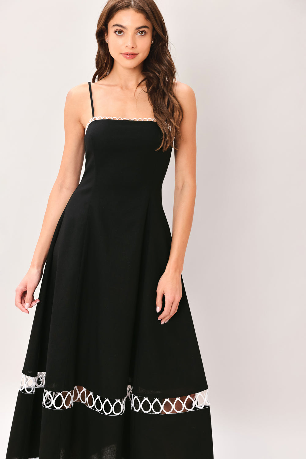 Woman wearing a black midi dress featuring straight neckline with lace edge trim, straps, circle skirt with lace inset bottom, lace edge trim and back zipper closure | Flying Tomato