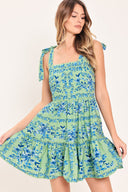 Woman wearing a green and blue floral mini dress featuring straight neckline, shoulder ties, ruffle hem and smocked back bodice with zipper closure | Flying Tomato