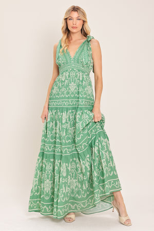 Woman wearing a sage green patterned maxi dress featuring V neckline, shoulder ties, tier skirt and smocked back waistband | Flying Tomato