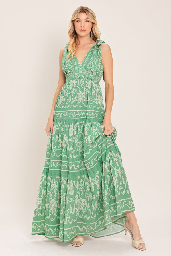 Woman wearing a sage green patterned maxi dress featuring V neckline, shoulder ties, tier skirt and smocked back waistband | Flying Tomato