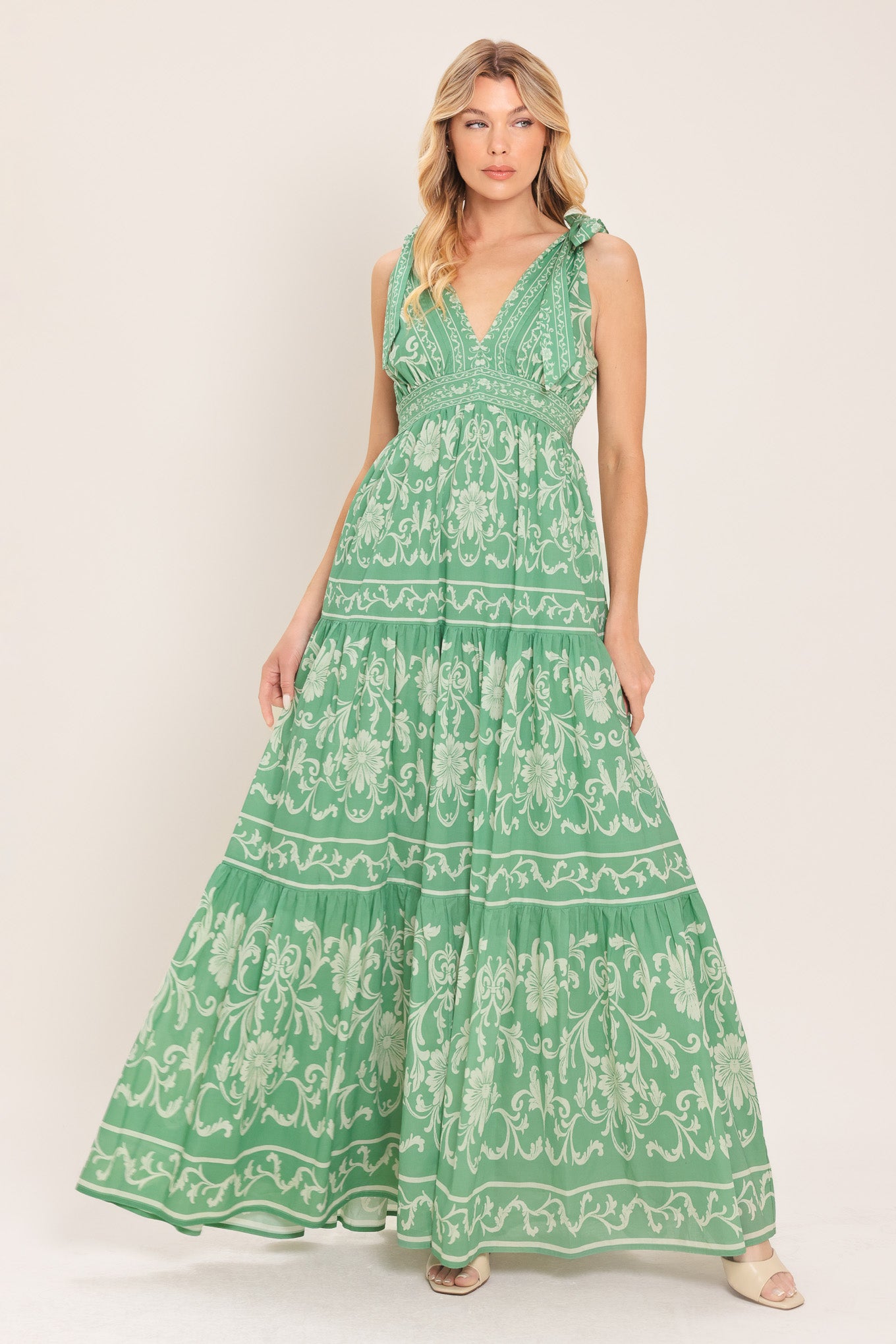 Woman wearing a sage green patterned maxi dress featuring V neckline, shoulder ties, tier skirt and smocked back waistband | Flying Tomato