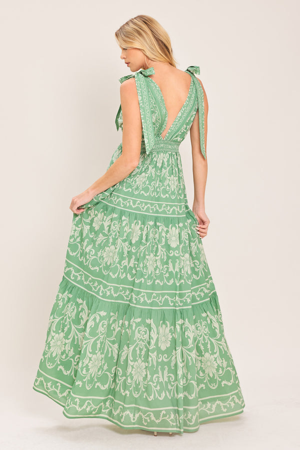 Woman wearing a sage green patterned maxi dress featuring V neckline, shoulder ties, tier skirt and smocked back waistband | Flying Tomato
