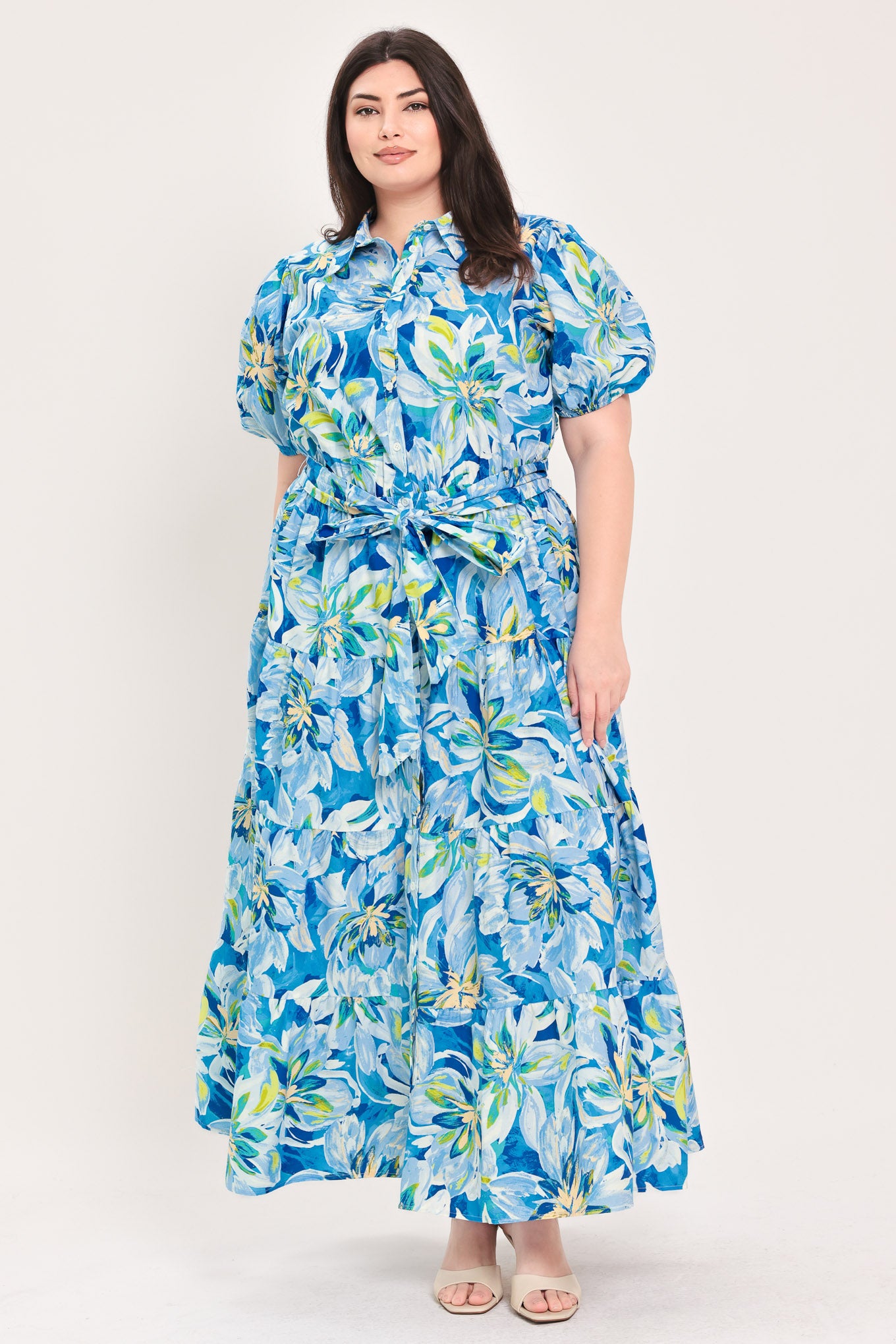 Woman wearing a blue floral midi dress featuring collar, short puff sleeve, button down, self-tie sash, tier skirt and pockets | Flying Tomato