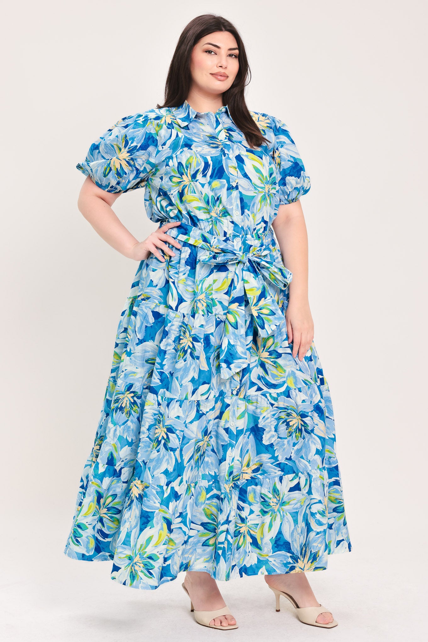 Woman wearing a blue floral midi dress featuring collar, short puff sleeve, button down, self-tie sash, tier skirt and pockets | Flying Tomato