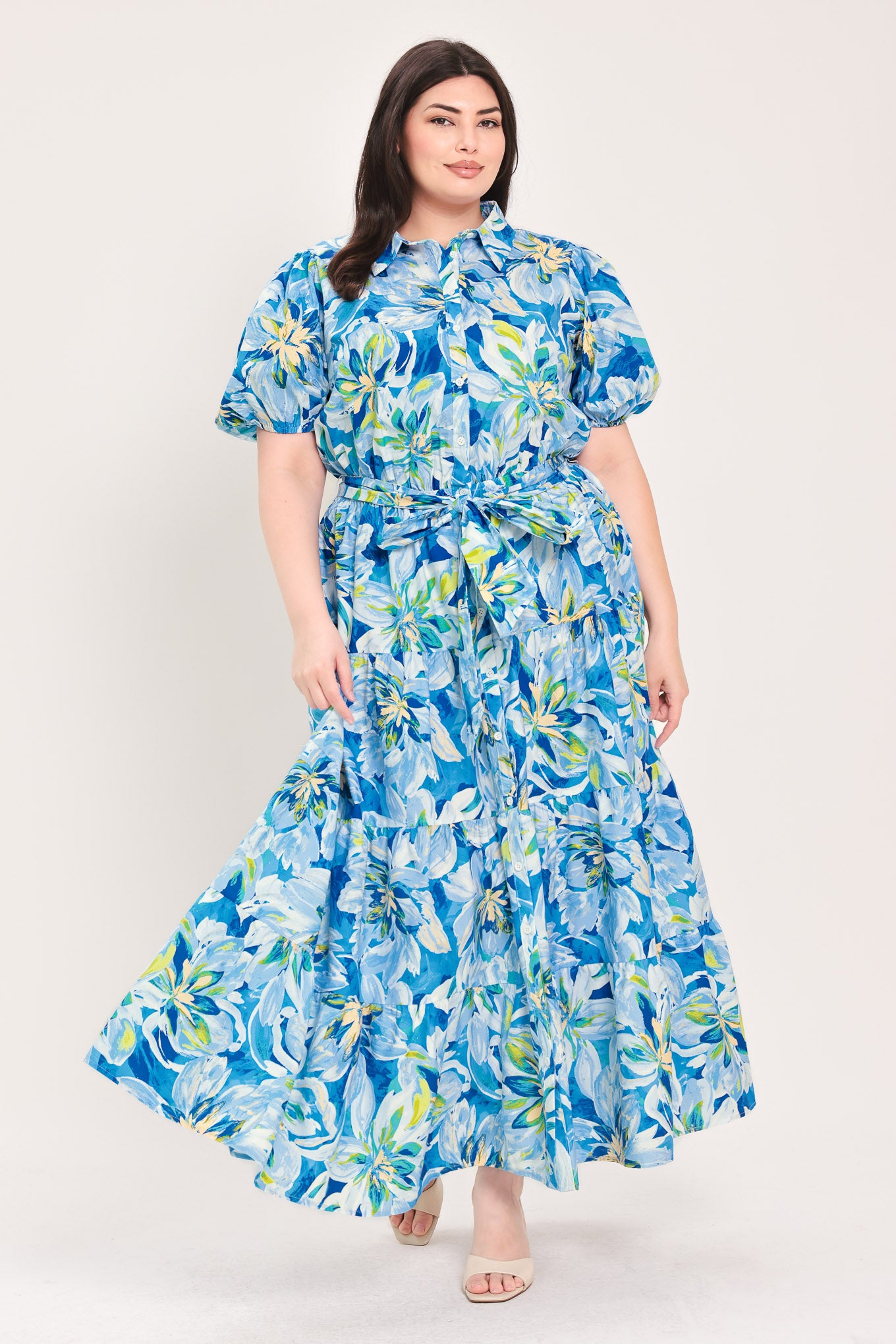 Woman wearing a blue floral midi dress featuring collar, short puff sleeve, button down, self-tie sash, tier skirt and pockets | Flying Tomato