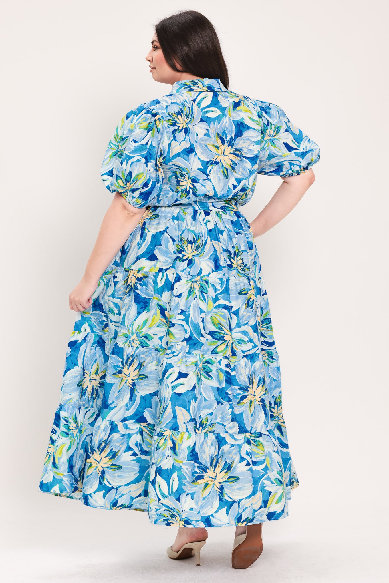 Woman wearing a blue floral midi dress featuring collar, short puff sleeve, button down, self-tie sash, tier skirt and pockets | Flying Tomato