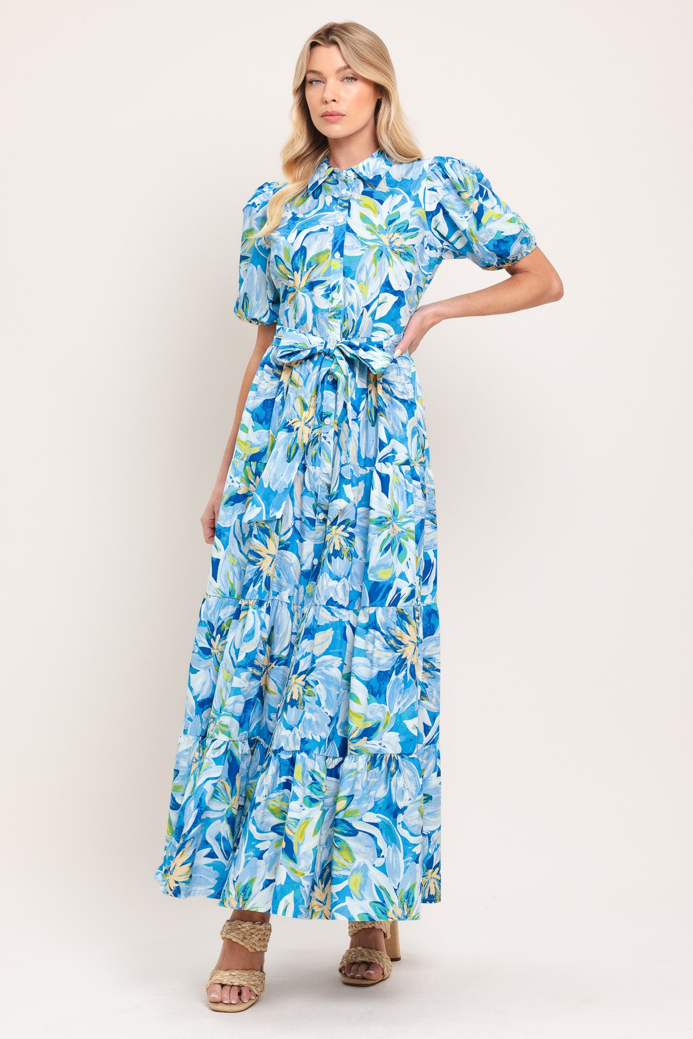 Woman wearing a blue floral midi dress featuring collar, short puff sleeve, button down, self-tie sash, tier skirt and pockets | Flying Tomato