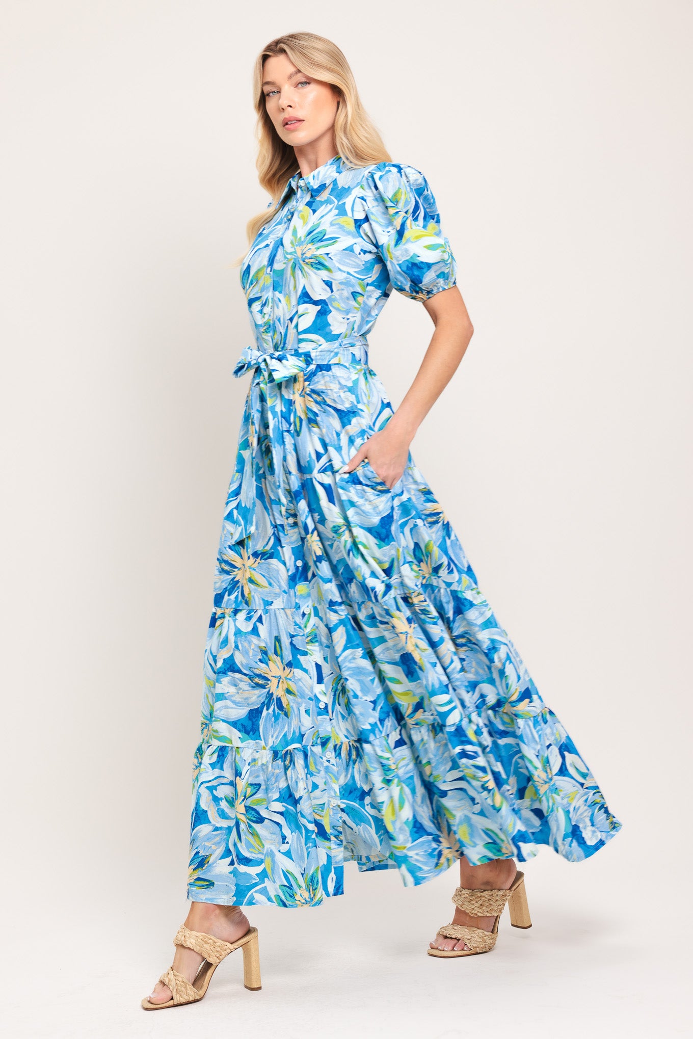 Woman wearing a blue floral midi dress featuring collar, short puff sleeve, button down, self-tie sash, tier skirt and pockets | Flying Tomato