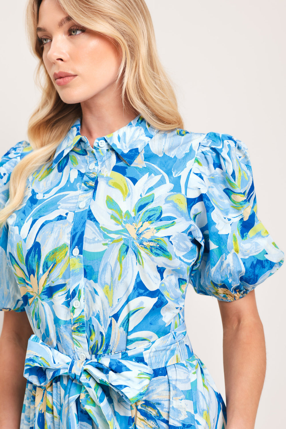 Woman wearing a blue floral midi dress featuring collar, short puff sleeve, button down, self-tie sash, tier skirt and pockets | Flying Tomato