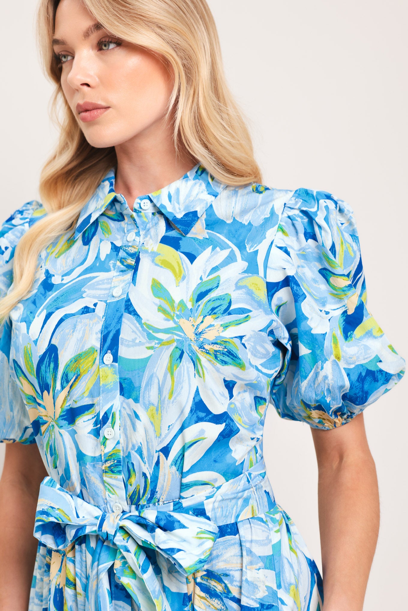 Woman wearing a blue floral midi dress featuring collar, short puff sleeve, button down, self-tie sash, tier skirt and pockets | Flying Tomato