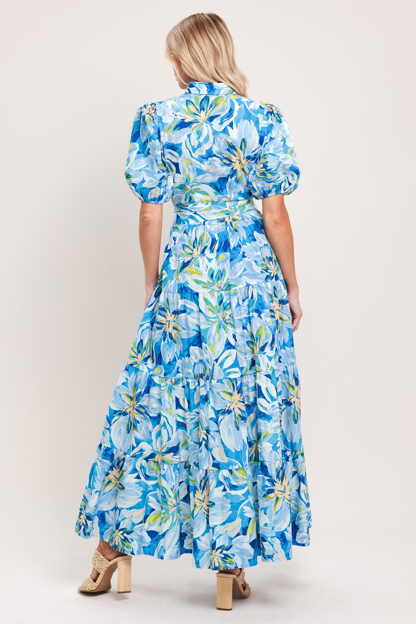 Woman wearing a blue floral midi dress featuring collar, short puff sleeve, button down, self-tie sash, tier skirt and pockets | Flying Tomato