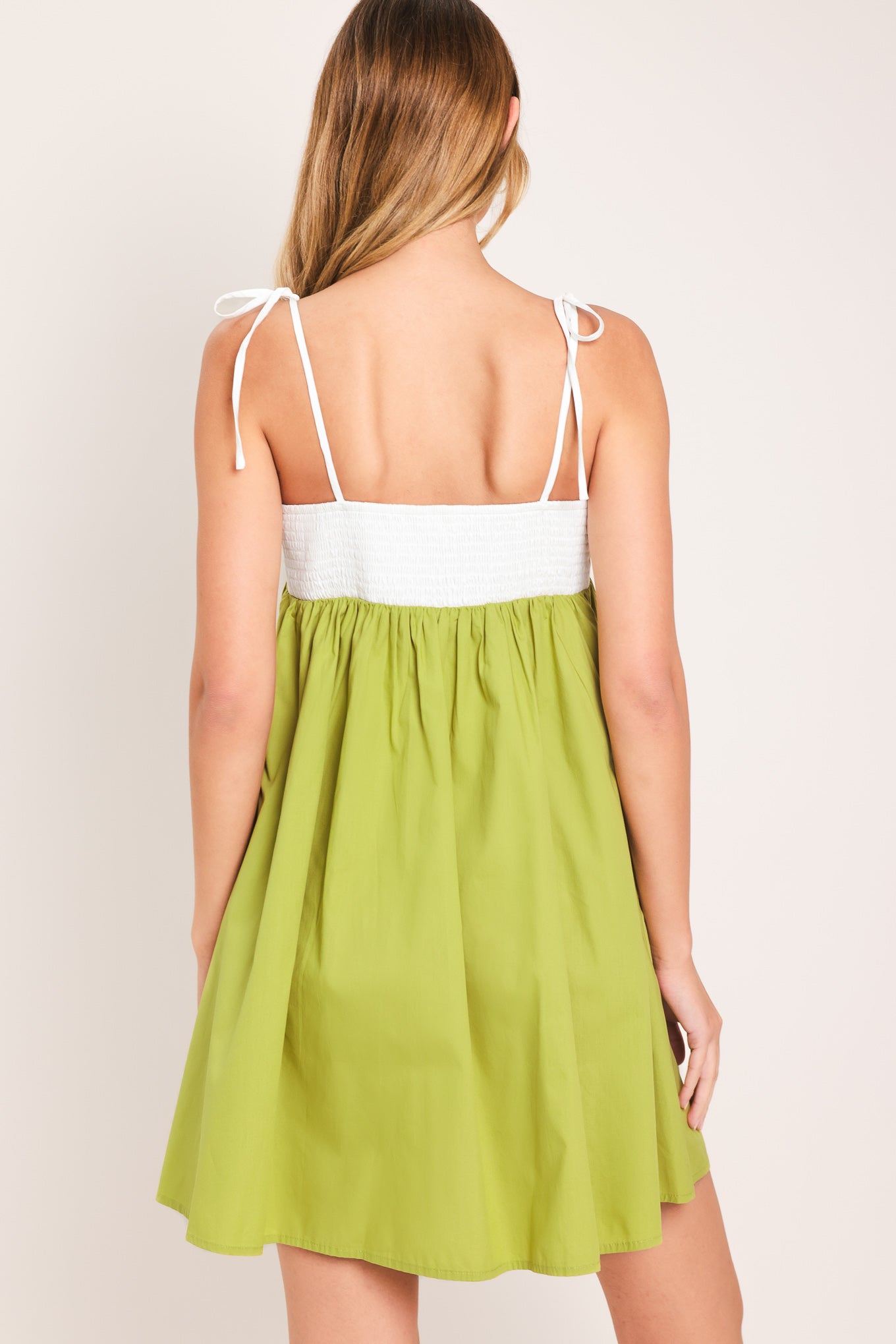 Woman wearing a white and green mini dress featuring straight neckline, straps and smocked back bodice | Flying Tomato