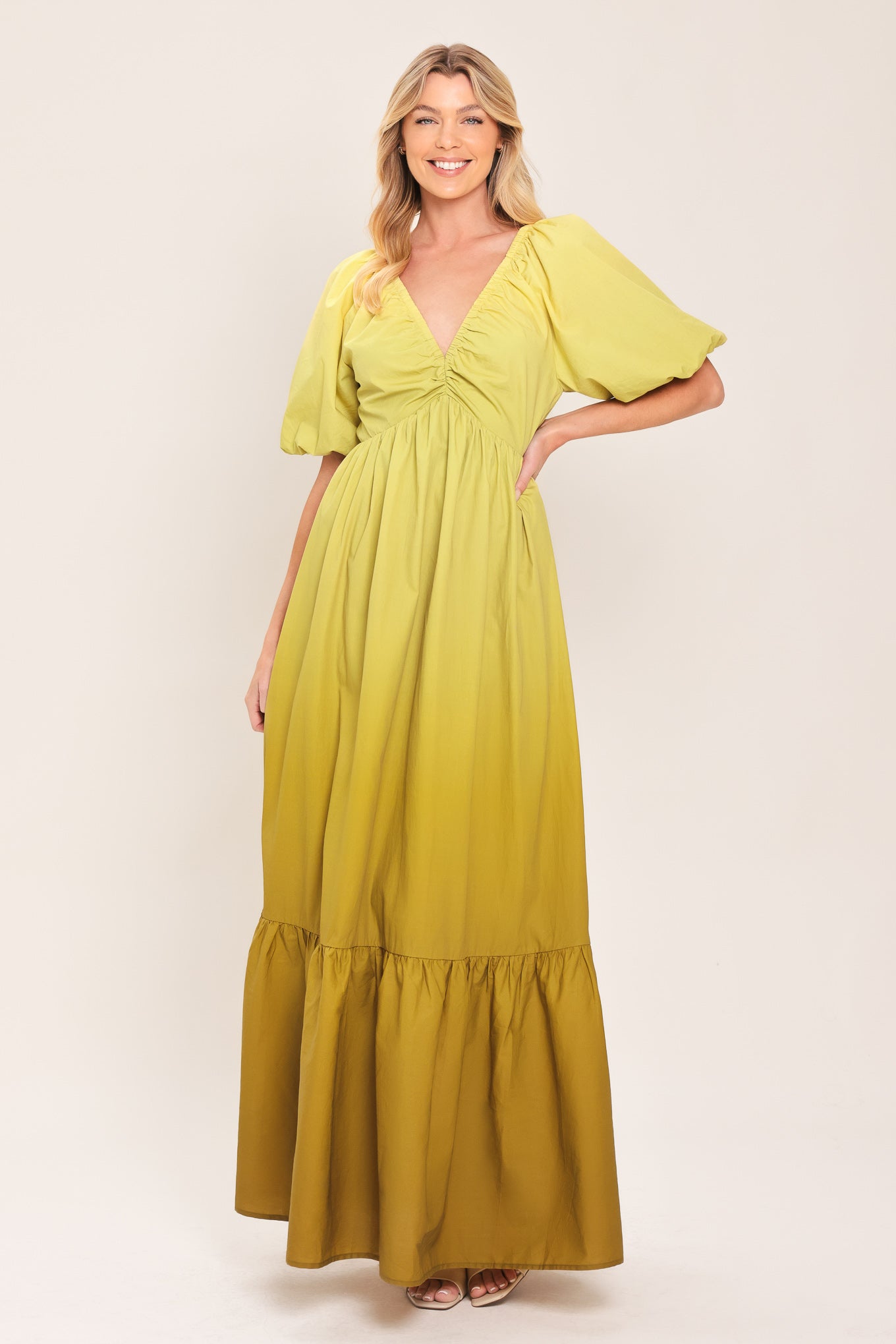 A woman wearing a yellow-green maxi dress with puff sleeves, a gathered V-neckline, and a tiered ruffle hem | Flying Tomato
