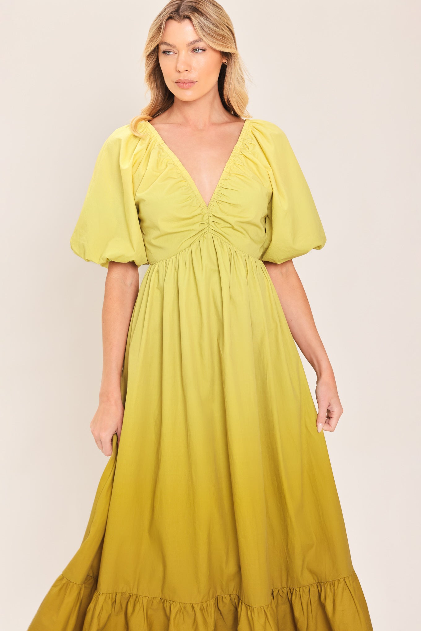 A woman wearing a yellow-green maxi dress with puff sleeves, a gathered V-neckline, and a tiered ruffle hem | Flying Tomato