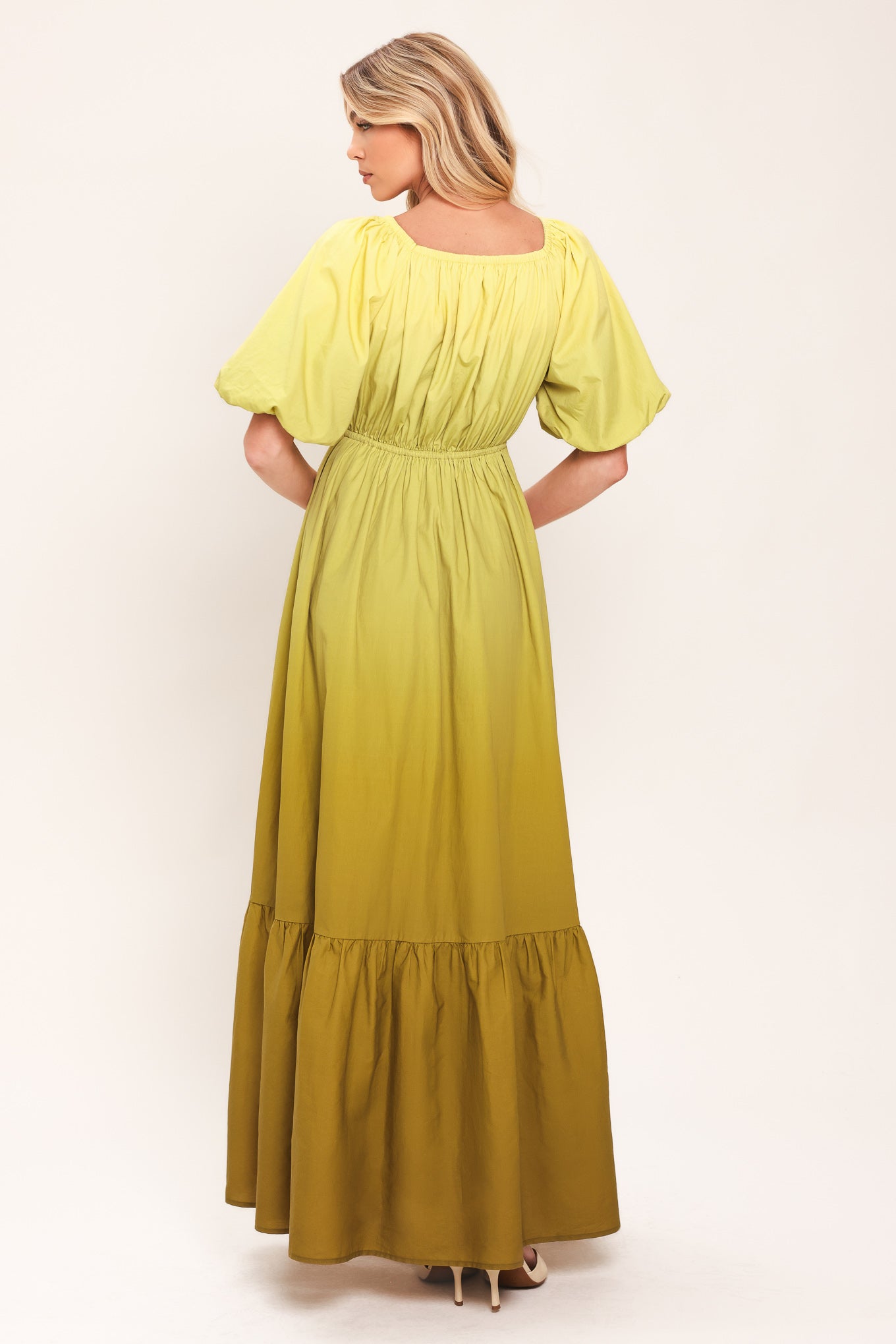 A woman wearing a yellow-green maxi dress with puff sleeves, a gathered V-neckline, and a tiered ruffle hem | Flying Tomato