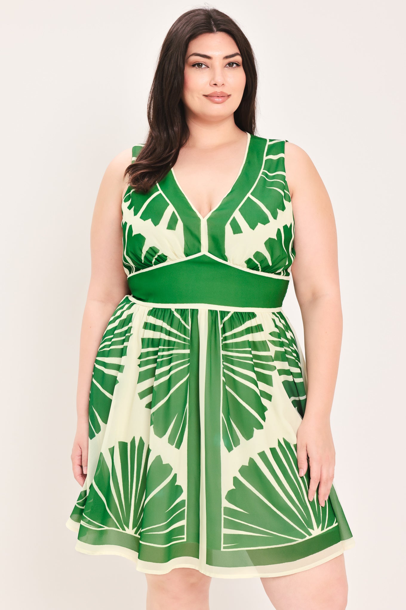 Woman wearing a sleeveless ivory with green leaf pattern mini dress featuring V neckline, full skirt and smocked back waistband | Flying Tomato
