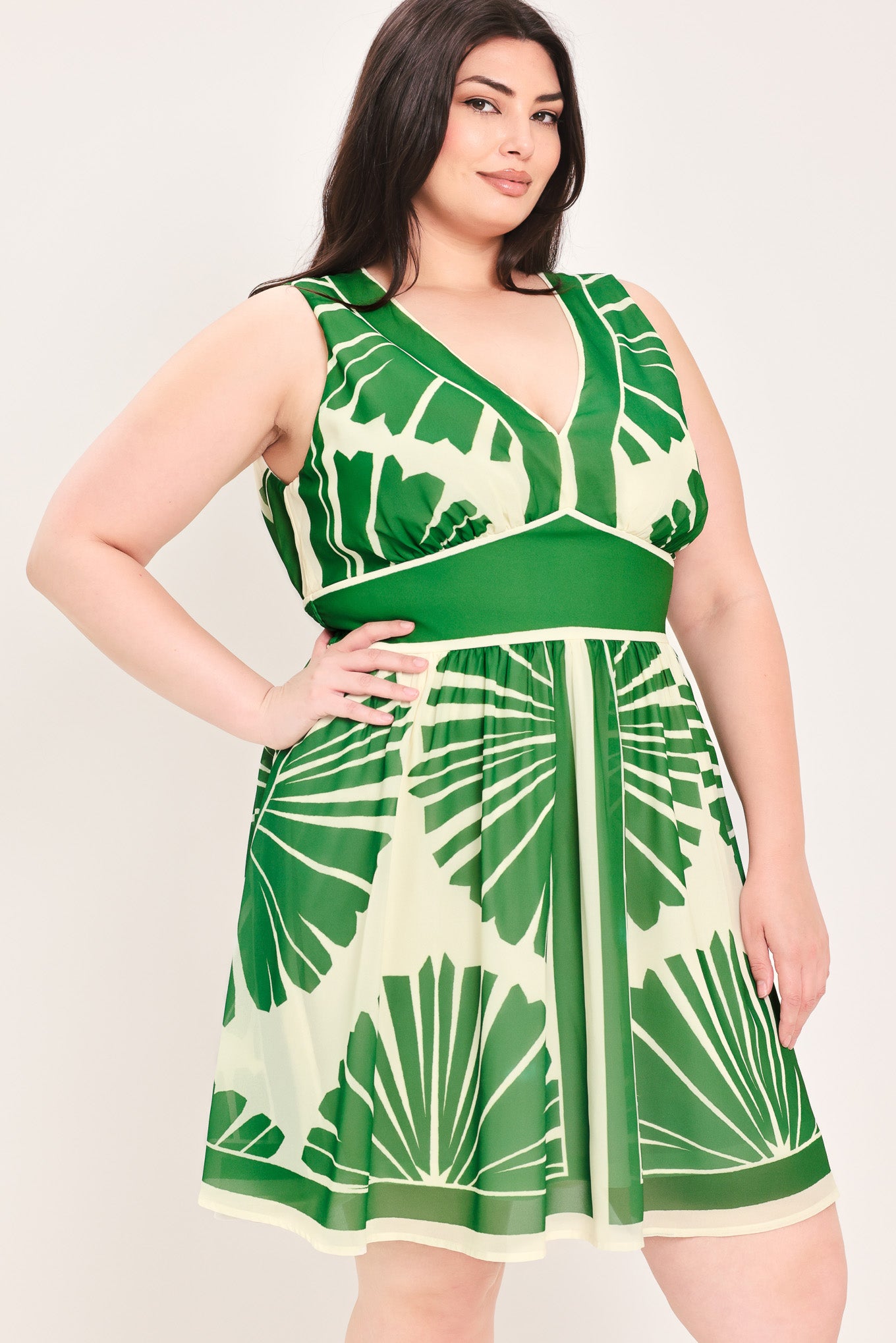 Woman wearing a sleeveless ivory with green leaf pattern mini dress featuring V neckline, full skirt and smocked back waistband | Flying Tomato