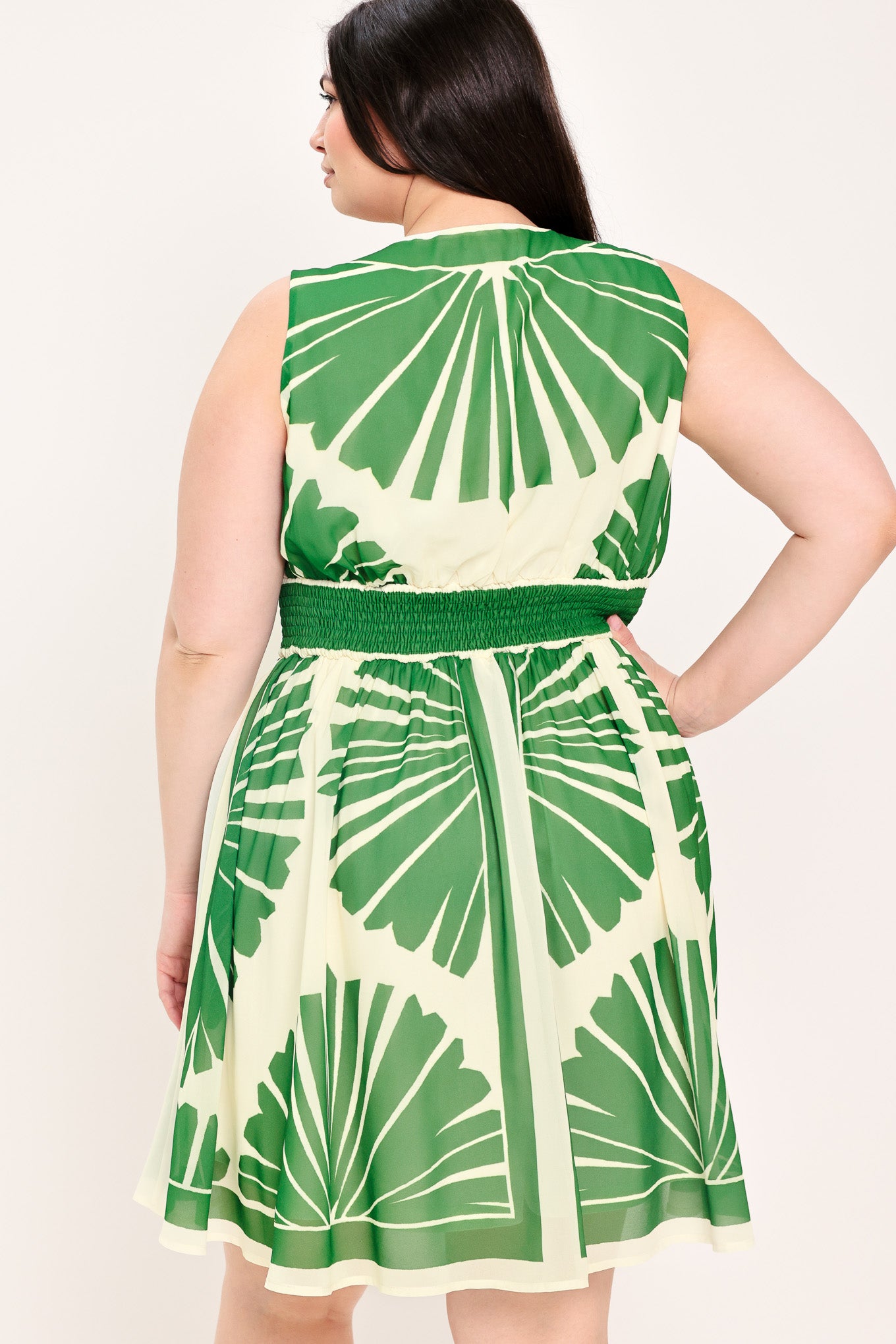 Woman wearing a sleeveless ivory with green leaf pattern mini dress featuring V neckline, full skirt and smocked back waistband | Flying Tomato