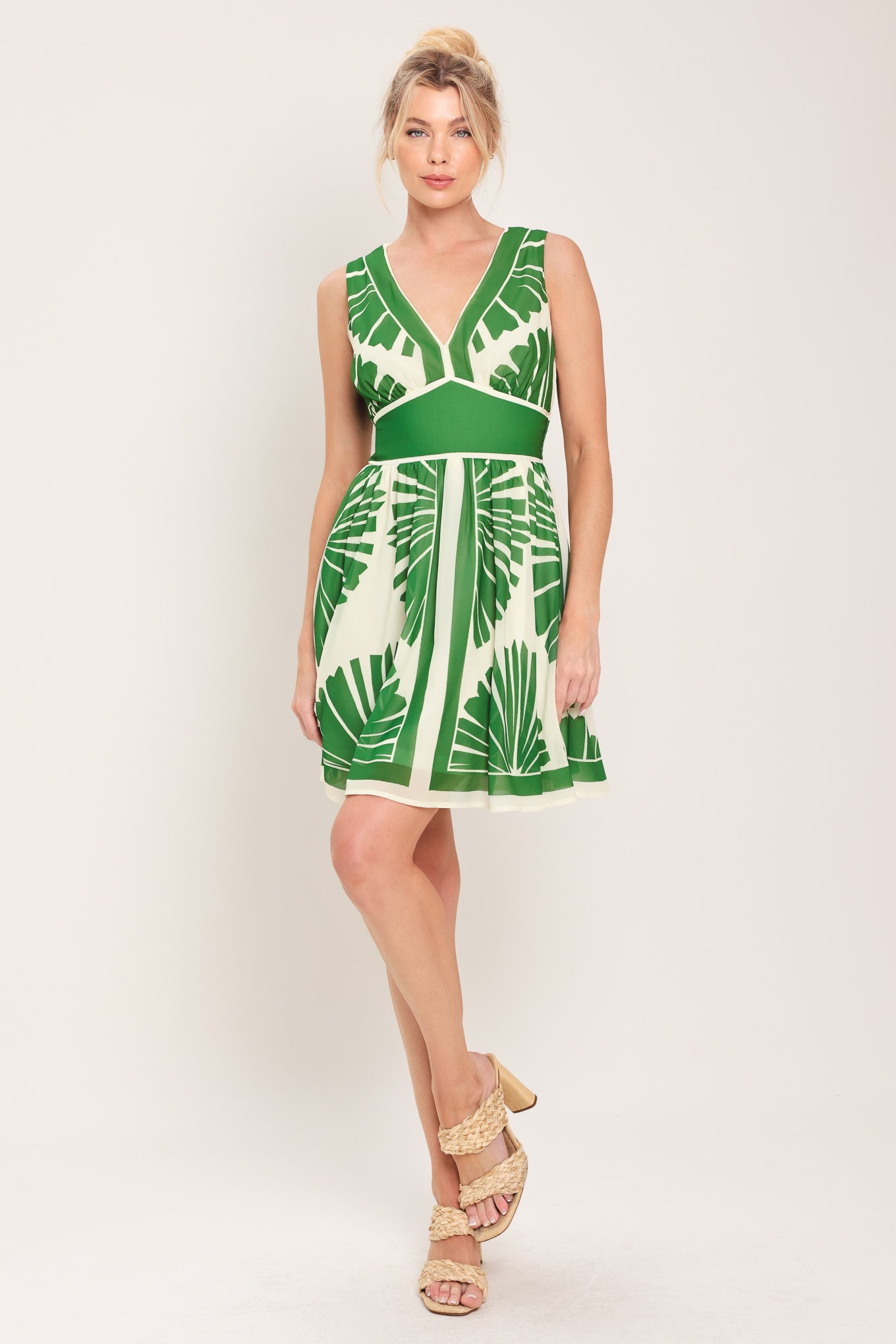 Woman wearing a sleeveless ivory with green leaf pattern mini dress featuring V neckline, full skirt and smocked back waistband | Flying Tomato
