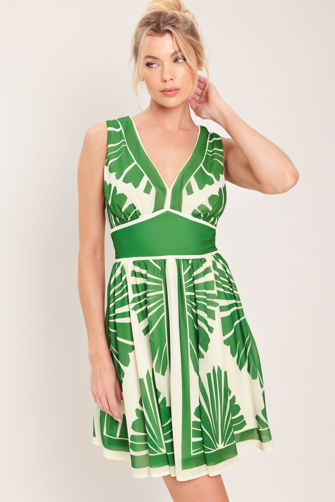 Woman wearing a sleeveless ivory with green leaf pattern mini dress featuring V neckline, full skirt and smocked back waistband | Flying Tomato