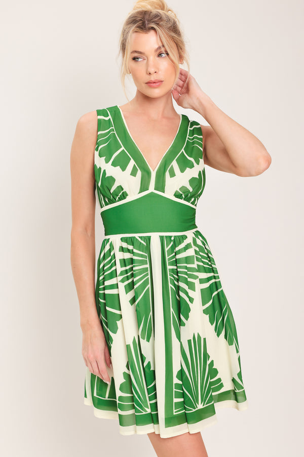 Woman wearing a sleeveless ivory with green leaf pattern mini dress featuring V neckline, full skirt and smocked back waistband | Flying Tomato
