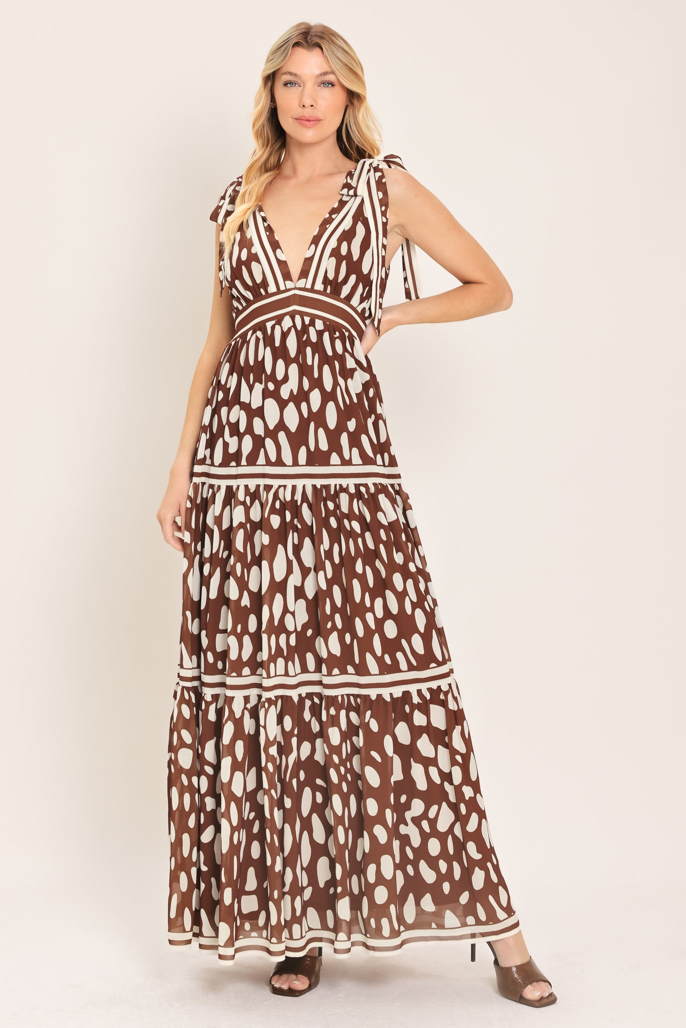 Woman wearing a brown and white spot patterned maxi dress featuring V neckline, shoulder ties, tier skirt and smocked back waistband | Flying Tomato