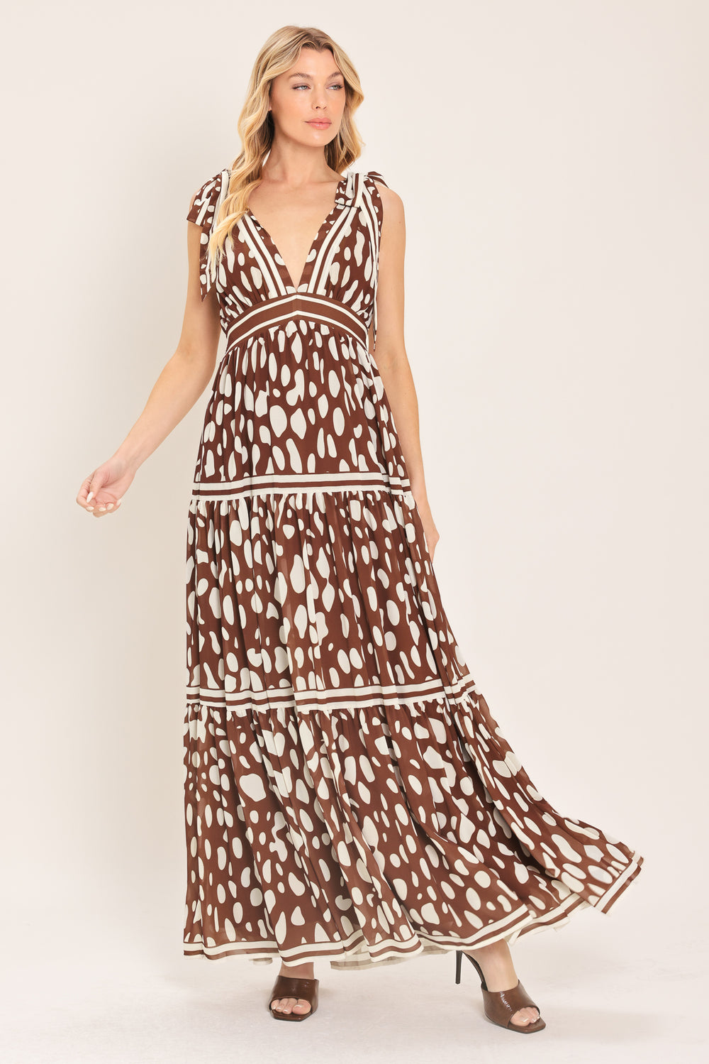 Woman wearing a brown and white spot patterned maxi dress featuring V neckline, shoulder ties, tier skirt and smocked back waistband | Flying Tomato
