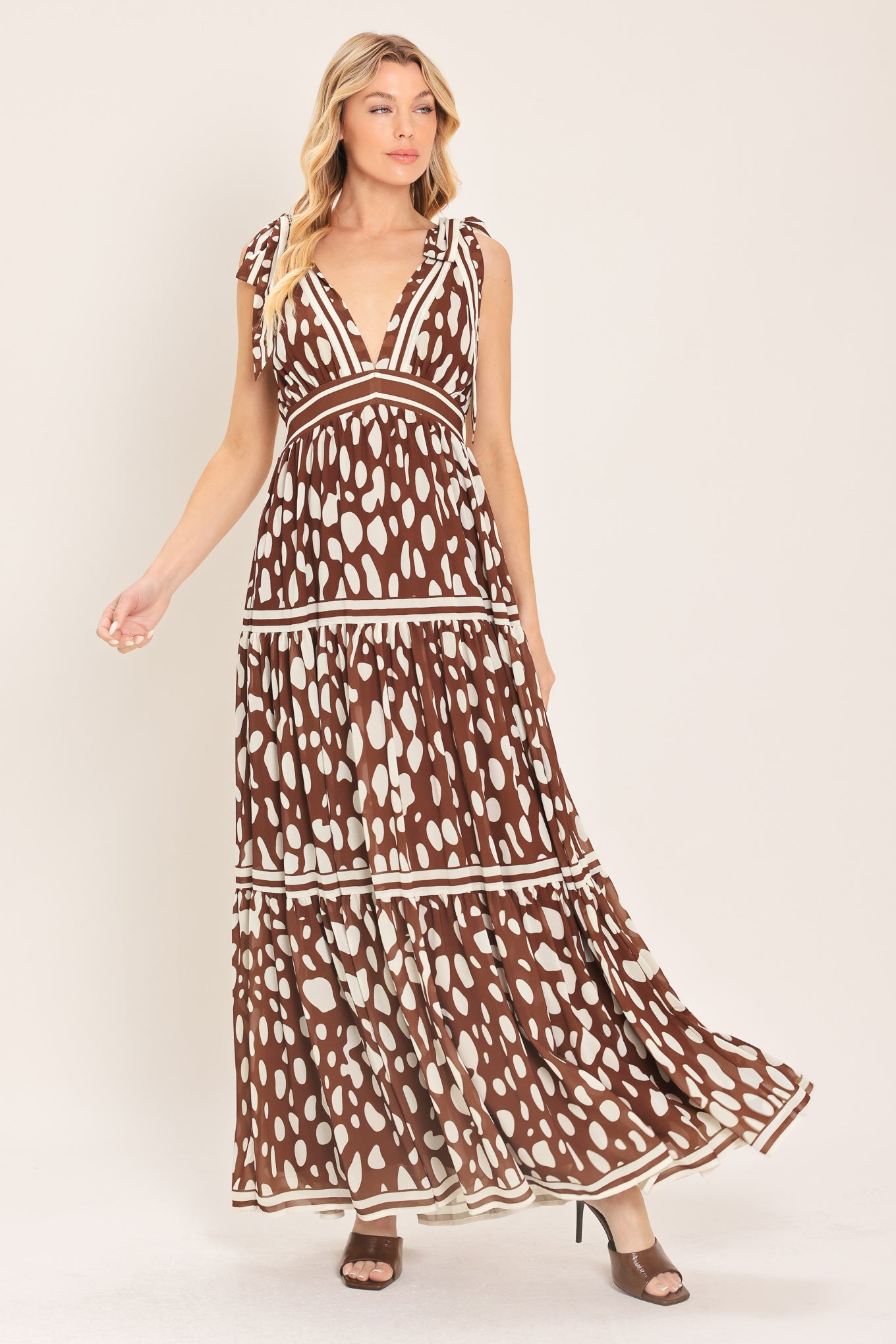 Woman wearing a brown and white spot patterned maxi dress featuring V neckline, shoulder ties, tier skirt and smocked back waistband | Flying Tomato