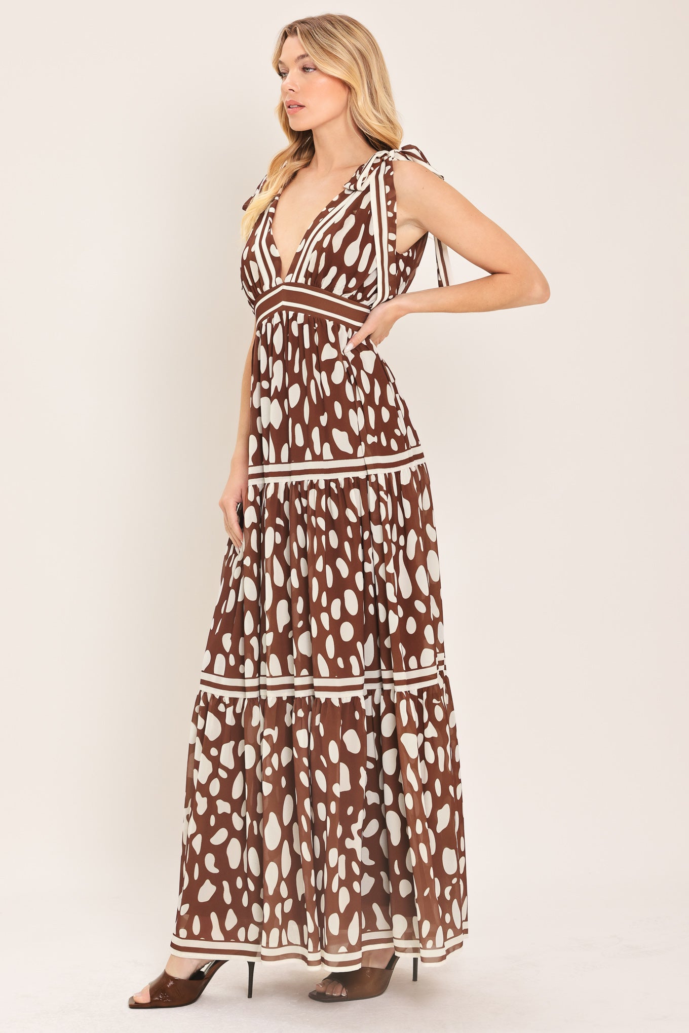 Woman wearing a brown and white spot patterned maxi dress featuring V neckline, shoulder ties, tier skirt and smocked back waistband | Flying Tomato