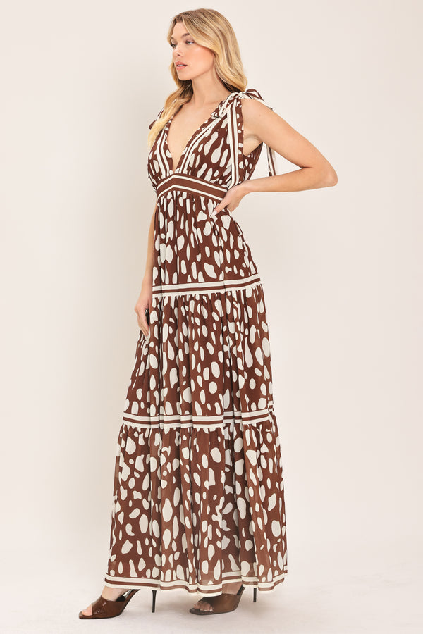 Woman wearing a brown and white spot patterned maxi dress featuring V neckline, shoulder ties, tier skirt and smocked back waistband | Flying Tomato