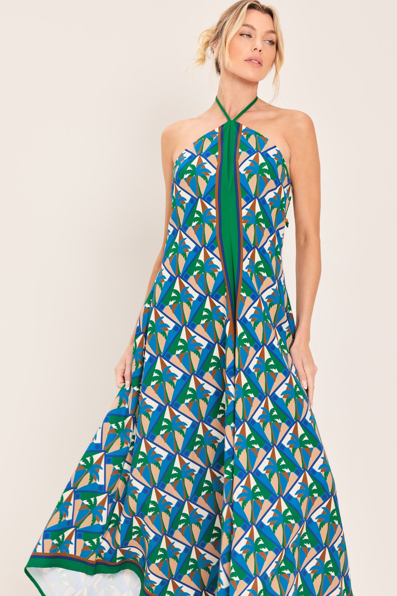 Woman wearing a colorful geometric patterned midi dress featuring halter neckline with tie, hanky hem and back zipper closure | Flying Tomato