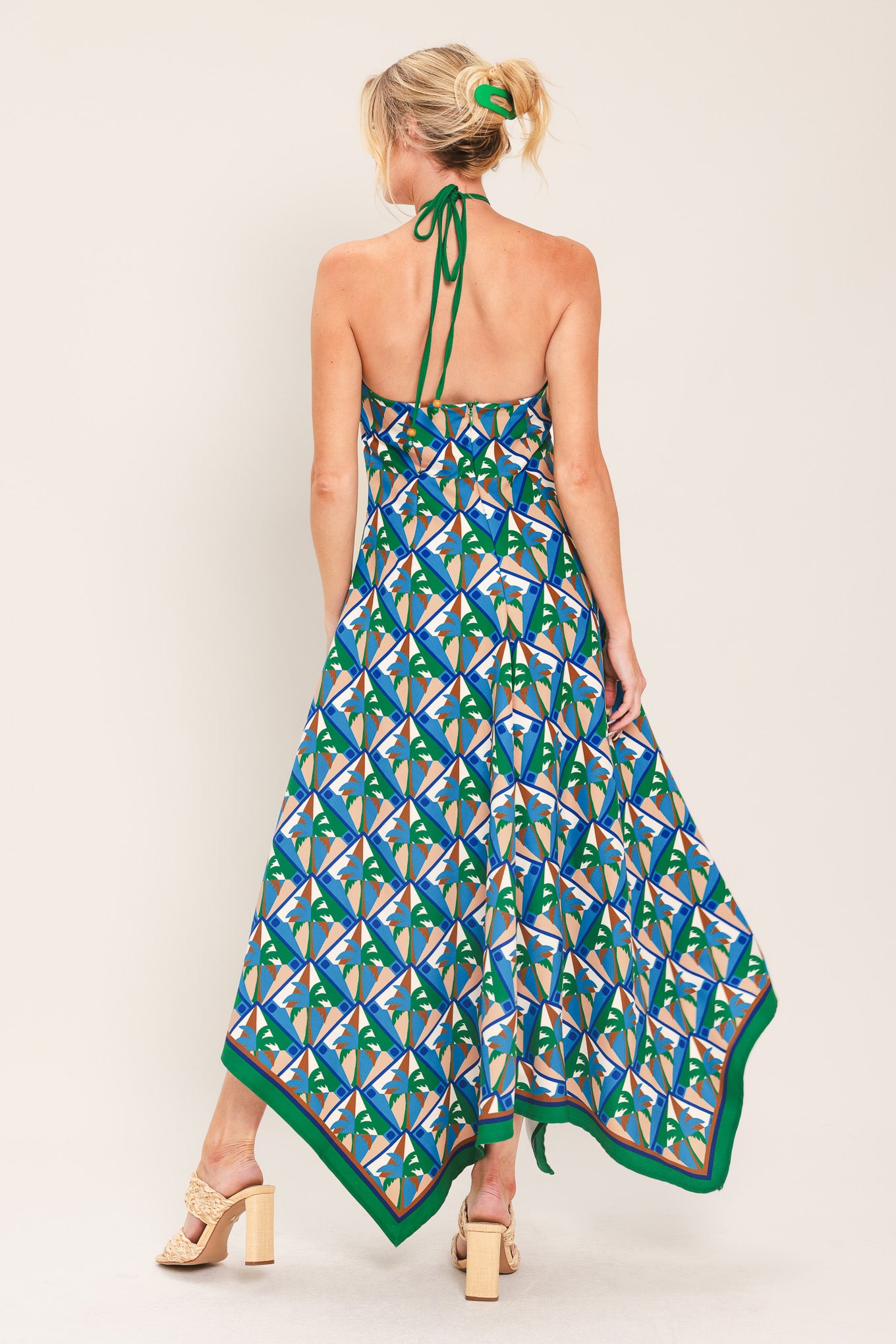 Woman wearing a colorful geometric patterned midi dress featuring halter neckline with tie, hanky hem and back zipper closure | Flying Tomato