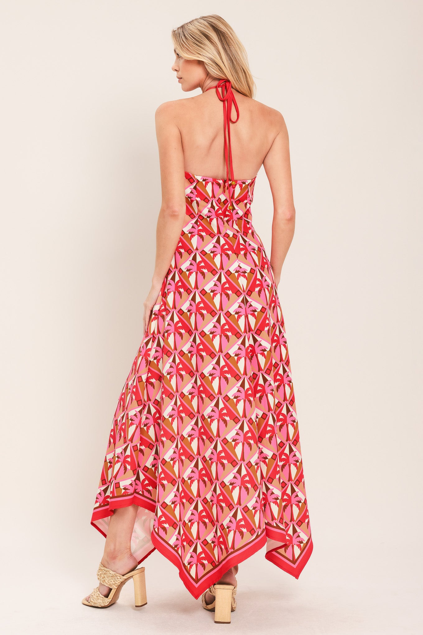 Woman wearing a colorful geometric patterned midi dress featuring halter neckline with tie, hanky hem and back zipper closure | Flying Tomato