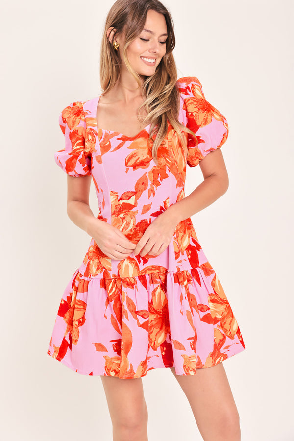 Woman wearing a lavender and coral floral printed mini dress featuring sweetheart neckline, short puff sleeve, ruffle hem and back zipper closure | Flying Tomato