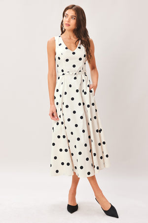 Woman wearing a white midi dress with black polka dots featuring V neckline, self belt, full circle skirt and back zipper closure | Flying Tomato