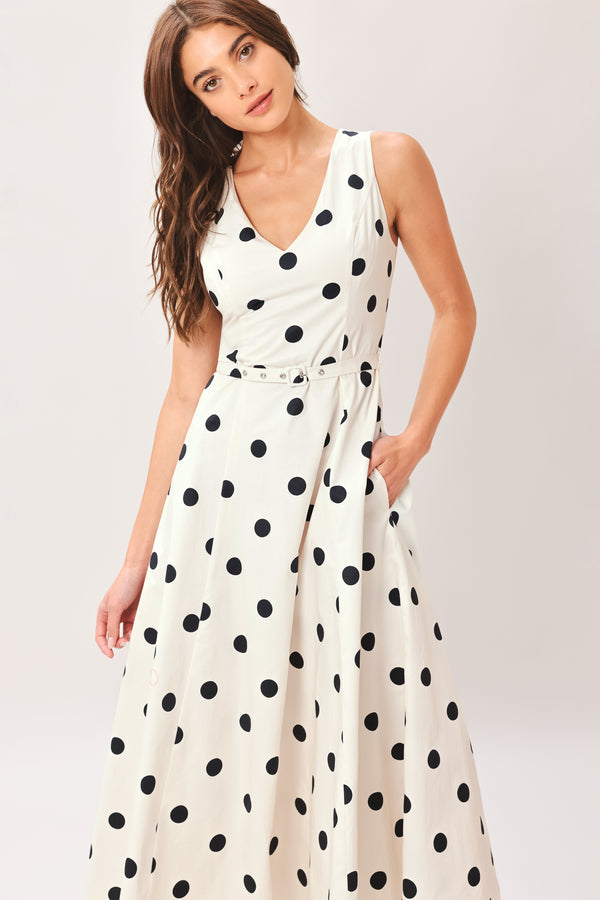 Woman wearing a white midi dress with black polka dots featuring V neckline, self belt, full circle skirt and back zipper closure | Flying Tomato
