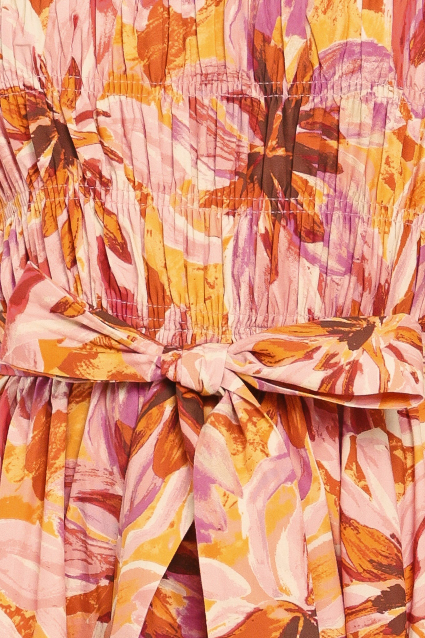Woman wearing a pink, yellow, and orange floral printed midi dress featuring ruffle neck with V center, short ruffle sleeve, wide smocked bodice, self sash tie and full skirt | Flying Tomato