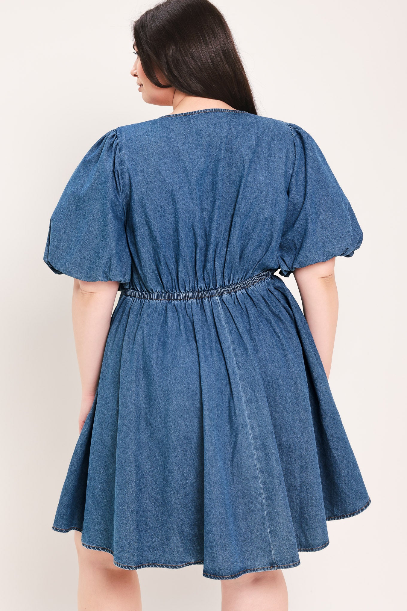 Woman wearing a denim mini dress featuring V neckline, short puff sleeve, button down detail, circle skirt and back zipper closure | Flying Tomato