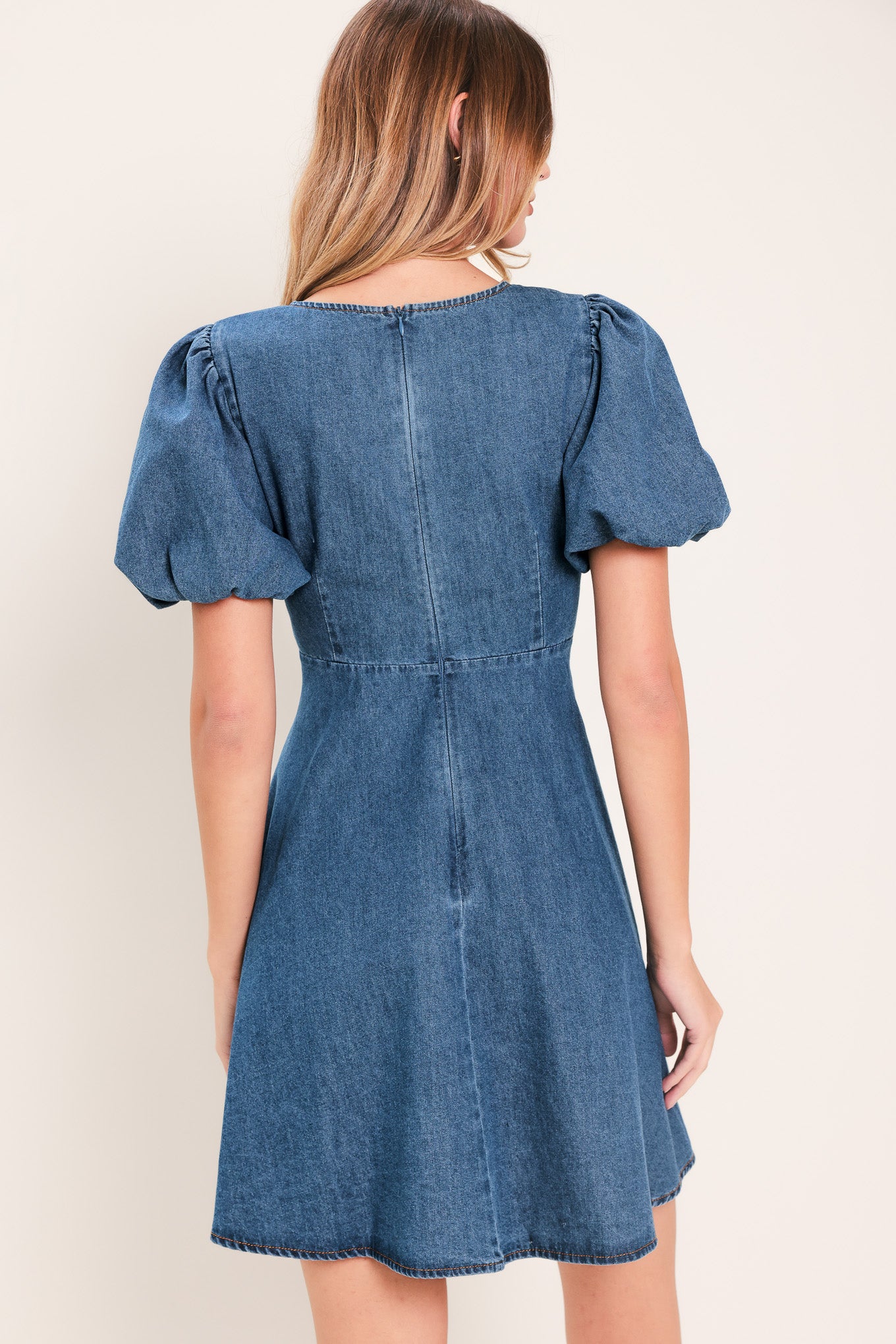 Woman wearing a denim mini dress featuring V neckline, short puff sleeve, button down detail, circle skirt and back zipper closure | Flying Tomato